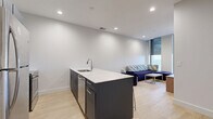 Located at 100 Clinton Square in downtown Rochester, NY, this well-appointed two-bedroom, one-bathroom unit offers a thoughtfully designed layout across a single floor. Light wood flooring flows consistently throughout the space, lending a bright, cohesive feel to every room.

The living room is a welcoming focal point, featuring floor-to-ceiling windows that frame sweeping elevated views of the Rochester cityscape. The space accommodates a sectional sofa with patterned cushions, a coffee table, and additional seating, all bathed in abundant natural light.

Each bedroom is equipped with a bed frame with built-in storage, a wardrobe cabinet, a desk, and an ergonomic chair. Large windows with roller shades offer both natural light and privacy, while the elevated vantage point provides impressive views of the surrounding city.

A connecting hallway with clean white walls and modern panel doors links the bedrooms to the shared bathroom. The bathroom features stylish navy-blue cabinetry, a white countertop vanity with a large mirror, an overhead storage cabinet, and distinctive white hexagonal tile flooring, creating a contemporary and functional space.

The overall design is modern and minimalist, with neutral tones, clean lines, and thoughtful furnishings that make efficient use of the available space throughout the unit.