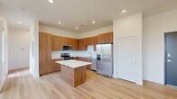 This well-designed single-story residence offers a thoughtful layout across one bedroom and one bathroom, blending modern finishes with a clean, contemporary aesthetic. The open-concept kitchen and living area forms the heart of the home, showcasing warm wood-grain cabinetry that extends floor to ceiling, stainless steel appliances including a French door refrigerator and range, and a central island with a crisp white countertop — ideal for both meal prep and casual dining. Light hardwood flooring runs throughout the main living space, enhancing the bright, airy atmosphere created by recessed lighting overhead. The generously sized bedroom features soft carpeting, a ceiling fan, and expansive windows that frame dramatic views of the surrounding red rock desert landscape, flooding the room with natural light. A secondary room with light hardwood flooring and large windows offers additional versatility and the same stunning desert scenery. The bathroom is finished with matching wood-tone cabinetry, a wide vanity with a white countertop, a large mirror, and light hardwood flooring, maintaining the cohesive, modern design language found throughout the residence. Clean white walls, consistent finishes, and an abundance of natural light give this space a calm, inviting character throughout.