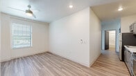 This single-floor unit offers a clean, contemporary design centered around an open-concept layout with light wood-style flooring that flows seamlessly through the main living areas. The kitchen is a standout feature, outfitted with grey shaker-style cabinetry, marble-look countertops, a white subway tile backsplash, and a full suite of stainless steel appliances including a range, microwave, and dishwasher. Recessed lighting illuminates the kitchen, which connects naturally to the adjacent living and dining area. The living space is equipped with a ceiling fan and a wall-mounted mini-split HVAC unit, ensuring year-round comfort. The bedrooms are finished with plush neutral carpeting and feature windows fitted with blinds that allow for ample natural light while maintaining privacy. Ceiling fans are present in the bedrooms, enhancing ventilation and comfort. The bathroom is neatly appointed with a full soaking tub and shower combination, brushed nickel fixtures, recessed lighting, and wood-look tile flooring that ties the space together. Throughout the unit, crisp white walls, clean baseboards, and a consistent neutral palette create a bright, welcoming ambiance ideal for a variety of furnishing styles.