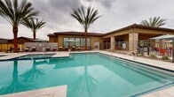 Located at 30825 N North Valley Pkwy in Phoenix, Arizona, this outdoor amenity area offers a resort-inspired pool environment designed for relaxation and recreation. The centerpiece is a generously sized swimming pool with clear turquoise water, featuring multiple entry points via built-in staircases and stainless steel handrails for convenient access. A separate spa is positioned adjacent to the main pool, providing a dedicated space for hydrotherapy. The surrounding pool deck is finished in light-toned pavers, creating a clean and polished aesthetic that complements the Arizona landscape. Tall, mature palm trees are strategically placed throughout the space, providing a tropical ambiance while offering partial shade. An extensive row of lounge chairs lines the perimeter, accompanied by market umbrellas for sun protection. Raised turf areas add visual contrast to the hardscape. A low-profile building with Southwest-inspired architecture, featuring stucco and stone accents, anchors one end of the space and likely provides restroom or facility access. The entire area is enclosed by a secure metal fence, ensuring privacy and safety. The overall atmosphere is open, bright, and well-suited to the warm Phoenix climate.