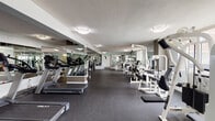 Located at 1450 Washington Blvd in Stamford, CT, this well-appointed fitness center offers a comprehensive workout environment across a single, expansive floor. The facility is organized into distinct functional zones, each designed to support a wide range of exercise modalities.

The main workout area is generously sized and lined with large mirrors that enhance the sense of space. A dedicated cardio zone houses a row of treadmills and elliptical machines, while an extensive strength training section features Cybex cable machines, weight benches, squat racks, and plate-loaded equipment. A well-stocked free weight area includes a full rack of dumbbells, weight plates, and flat mats for floor exercises.

Natural light filters in through multiple windows throughout the space, providing views of the surrounding neighborhood. The flooring throughout is a durable, dark rubber material suited for high-impact use.

A separate functional training room offers additional versatility, equipped with exercise mats, resistance bands, a punching bag, stability balls, medicine balls, and a wall-mounted flat-screen TV. This room also benefits from its own window, maintaining the bright, open feel consistent with the rest of the facility.

The overall design is clean and modern, with neutral gray and white tones creating a focused and professional training atmosphere.