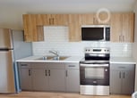 This 310 square foot studio apartment in Duluth offers a thoughtfully designed living space that maximizes functionality within its compact footprint. The open-concept layout seamlessly integrates the living area, kitchen, and sleeping space, creating a sense of spaciousness despite the limited square footage.

The kitchen is a standout feature, boasting a sleek and modern design. It's equipped with stainless steel appliances, including a full-sized refrigerator, range, and built-in microwave. The cabinetry combines light wood upper cabinets with gray lower cabinets, providing ample storage. White subway tile backsplash and quartz countertops add a touch of elegance.

The bathroom, while compact, is well-appointed with a modern vanity featuring a wood cabinet, white countertop, and a large circular mirror. A glass-enclosed shower (not visible in images) is likely present. The water heater is conveniently tucked away in the bathroom.

Throughout the apartment, warm wood-look flooring creates a cohesive and inviting atmosphere. Large windows in the main living area flood the space with natural light, enhancing the sense of openness. The neutral color palette of whites and light grays on the walls contributes to the bright, airy feel of the space.

Recessed lighting fixtures provide additional illumination, ensuring the apartment remains well-lit even after dark. While the space is limited, its efficient design and modern amenities make it an attractive option for those seeking a contemporary urban living experience in a compact package.