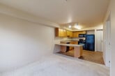 This one-bedroom, one-bathroom unit at 1140 N 192nd St in Shoreline, WA offers a thoughtfully designed single-floor layout that maximizes every inch of its compact footprint. The open-concept main living area seamlessly integrates the living room, dining space, and kitchen, creating a cohesive and functional environment. The kitchen is well-appointed with warm honey-toned wood cabinetry, generous upper and lower storage, a peninsula countertop that doubles as a breakfast bar, and black appliances including a refrigerator, range, dishwasher, and over-the-range microwave. Track lighting overhead and a recessed skylight-style fixture illuminate the kitchen efficiently. Light hardwood-style flooring runs through the kitchen and entry areas, transitioning to plush carpet in the living and bedroom spaces. The bedroom is a comfortable, carpeted retreat featuring a large window that allows natural light to filter in, a baseboard heater, and a sliding double-door closet alongside an additional closet for ample storage. The bathroom is clean and straightforward, finished with wood-toned cabinetry, a single vanity, and wood-look flooring. Neutral warm beige tones throughout the unit create a calm, cohesive ambiance.