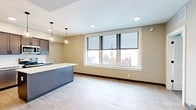 Located at 24 Bank Pl in Utica, NY, this thoughtfully designed one-bedroom, one-bathroom unit offers a comfortable and modern living experience across a single floor. The open-concept layout connects the kitchen and living area seamlessly, creating an efficient and welcoming atmosphere throughout.

The kitchen is a standout feature, showcasing rich dark cabinetry with a classic white subway tile backsplash, light quartz countertops, and a central island with pendant lighting overhead. Stainless steel appliances — including a refrigerator, electric range, microwave, and dishwasher — complete this well-appointed space. Light hardwood-style flooring runs throughout the main living area, enhancing the bright and airy feel.

A large multi-pane window in the living area frames views of the surrounding Utica cityscape, allowing abundant natural light to pour in. In-unit laundry is also conveniently included.

The bedroom features soft carpeting, cool sage-toned walls, and a dedicated closet with built-in rod storage. The bathroom is clean and functional, offering a full tub-shower combination with white tile surround, oil-rubbed bronze fixtures, and a vanity with granite countertop and tile flooring. The unit's modern finishes and practical layout make it an ideal space in the heart of downtown Utica.