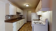 This single-floor residence offers a practical and comfortable layout across several well-defined living spaces. The galley-style kitchen is a functional highlight, featuring white cabinetry with ample upper and lower storage, dark laminate countertops, and a mosaic tile backsplash in warm earth tones. White appliances include a gas range and a full-size refrigerator, complemented by an under-cabinet range hood and a built-in dishwasher. Wood-look flooring runs throughout the kitchen, adding warmth to the space. The living room is generously sized, finished with plush carpeting, a textured ceiling, and a large sliding glass door that opens to a private balcony, inviting natural light and outdoor views. The bedroom offers soft carpeting, a ceiling fan with light fixture, a closet, and a broad window framing exterior views. An additional room with carpeting and a ceiling-mount light fixture provides flexible use as a second bedroom or den. The bathroom includes a full soaking tub with white tile surround, a toilet, and a vanity with countertop, all framed by warm wood-toned door trim. Throughout the unit, baseboard heating, neutral wall tones, and wood-accented trim details contribute to a cohesive and livable aesthetic.