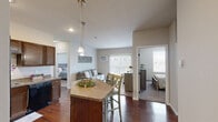 Located at 3709 7th St W in Williston, North Dakota, this 2-bedroom, 2-bathroom single-floor residence offers a well-designed layout that maximizes comfort and functionality. The open-concept kitchen serves as the heart of the home, outfitted with rich dark wood cabinetry, granite-style countertops, black appliances including a refrigerator, range, microwave, and dishwasher, and a central island with bar seating illuminated by pendant lighting. Durable hardwood-style flooring flows throughout the kitchen and dining areas, adding warmth and visual continuity. The adjoining living room features soft carpeting, a wall-mounted air conditioning unit, and access to natural light through large windows with vertical blinds. Both bedrooms are carpeted and offer a calm, neutral palette with ample natural light from well-placed windows. The primary bedroom includes its own closet, and the space benefits from a total of four closets throughout. Each of the two full bathrooms includes a tub-shower combination, a vanity with dark wood cabinetry and stone-style countertops, and hardwood-style flooring. The overall design is clean and cohesive, with neutral tones and practical finishes that create a comfortable, move-in-ready living environment.