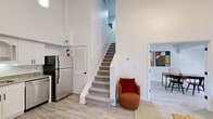 Located at 1000 Navaho Dr in Raleigh, NC, this two-story residence offers a well-organized layout across two floors, combining functional design with a bright, modern aesthetic. Light wood-style flooring and crisp white walls flow throughout, creating a clean and airy atmosphere.

The main floor houses the kitchen, dining room, and living room. The kitchen is outfitted with white shaker cabinetry, granite countertops, stainless steel appliances — including a refrigerator, dishwasher, range, and built-in microwave — and a matte black faucet at the sink. The dining area accommodates a full dining table and is brightened by a window with patterned curtains. The living room impresses with soaring double-height ceilings, a decorative fireplace surround, and natural light from a window, lending a sense of openness well beyond the floor's footprint. A carpeted staircase connects the two levels.

Upstairs, the primary bedroom is a comfortable retreat featuring a closet, a window with natural light, and direct access to a bathroom with a tub-shower combination. A second bathroom serves the home as well. The upper floor's more intimate scale balances the grand volume of the main living area, making this a distinctive and efficiently designed two-story home.