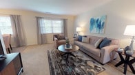 Located at 744 Eayrestown Rd in Lumberton, New Jersey, this single-floor residence offers a well-organized and functional layout with comfortable living spaces throughout. The living room is bright and inviting, featuring plush carpeting, a large window with draping curtains that allow natural light to fill the room, and ample space for seating. Adjacent to the living area is a dedicated dining space, finished with hard-surface flooring and a classic chandelier overhead, alongside a window that adds to the room's natural brightness. The kitchen is efficiently laid out in an L-shape, featuring white cabinetry, light countertops, and full appliances including a refrigerator, electric range, and dishwasher. The bedroom is generously sized with soft carpeting, a large window, and a sliding-door closet, providing comfortable and practical accommodations. A hallway bathroom includes tile flooring, a single-sink vanity with a large mirror, and direct access to the main living area. Throughout the residence, warm neutral tones on the walls and light-colored carpeting create a cohesive and welcoming ambiance, making this a well-appointed and move-in ready home.
