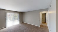 This single-floor residence offers a practical and well-organized layout finished in neutral, warm-toned décor throughout. The living area is spacious and carpeted, featuring large sliding glass doors dressed with vertical blinds that allow generous natural light and provide outdoor views. The space flows openly into an adjacent area, also carpeted and equipped with a ceiling fan, suitable for use as a dining or secondary living space.

The bedrooms are carpeted and bathed in natural light through blinds-covered windows. The primary bedroom is notably well-appointed, featuring two sets of double panel closets that provide substantial storage. A second bedroom offers a similar calm aesthetic with its own window and ample floor space.

The galley-style kitchen is efficiently arranged with gray cabinetry lining both sides, light countertops, a double-basin sink, and wood-look flooring. Black appliances include a refrigerator, range, dishwasher, and over-the-range microwave, offering a complete set of essentials within a compact, functional footprint.

The bathroom includes a wide vanity with a single basin, light countertop, gray cabinetry beneath, a large mirror with overhead lighting, and a tub-shower combination. Consistent neutral wall tones and white trim carry throughout, giving the entire space a cohesive and clean appearance.