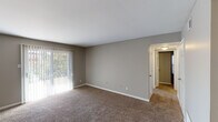This single-floor residence offers a practical and well-organized layout finished in neutral, warm-toned décor throughout. The living area is spacious and carpeted, featuring large sliding glass doors dressed with vertical blinds that allow generous natural light and provide outdoor views. The space flows openly into an adjacent area, also carpeted and equipped with a ceiling fan, suitable for use as a dining or secondary living space.

The bedrooms are carpeted and bathed in natural light through blinds-covered windows. The primary bedroom is notably well-appointed, featuring two sets of double panel closets that provide substantial storage. A second bedroom offers a similar calm aesthetic with its own window and ample floor space.

The galley-style kitchen is efficiently arranged with gray cabinetry lining both sides, light countertops, a double-basin sink, and wood-look flooring. Black appliances include a refrigerator, range, dishwasher, and over-the-range microwave, offering a complete set of essentials within a compact, functional footprint.

The bathroom includes a wide vanity with a single basin, light countertop, gray cabinetry beneath, a large mirror with overhead lighting, and a tub-shower combination. Consistent neutral wall tones and white trim carry throughout, giving the entire space a cohesive and clean appearance.