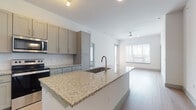 This single-floor unit offers a thoughtfully designed open-concept layout where the kitchen flows seamlessly into the living area, creating a bright and connected living space. The kitchen is a standout feature, showcasing grey shaker-style cabinetry, granite countertops, a white island with a stainless steel undermount sink, and a full suite of stainless steel appliances including a refrigerator with ice maker, electric range, and built-in microwave. A classic white subway tile backsplash adds a clean, modern touch.

The living area benefits from generous natural light through large windows dressed with horizontal blinds, and is finished with a ceiling fan overhead. Wood-look plank flooring runs consistently throughout the unit, providing warmth and a cohesive aesthetic.

The bedrooms are bright and well-proportioned, each featuring large windows with outdoor views and the same warm wood-look flooring. The primary suite connects to a spacious bathroom equipped with a granite-topped double vanity with grey cabinetry, a glass-enclosed shower, and an adjoining walk-in closet with built-in shelving and hanging rods. The clean, neutral color palette of white walls and grey accents lends the entire unit a contemporary, move-in-ready feel.