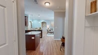 This thoughtfully designed single-floor residence combines modern finishes with a warm, inviting atmosphere. The open-concept kitchen serves as a centerpiece, showcasing rich dark-wood cabinetry, granite countertops, stainless steel appliances, and a central island with pendant lighting overhead. Crown molding and arched architectural details add a refined touch, while light wood-style flooring flows seamlessly into the connected living area. The living space is bright and welcoming, featuring crown molding, neutral tones, and natural light filtering through window treatments. An arched passageway connects the living and dining areas, enhancing the open flow of the layout. The primary bedroom offers a serene retreat with plush carpeting, a ceiling fan, and soft, neutral walls. Its en-suite bathroom is equipped with a granite-topped dark-wood vanity, a dedicated vanity seating area, and tile flooring. The second bedroom mirrors the comfort of the primary, with hardwood-style flooring and generous natural light from a large window. A second full bathroom features a granite vanity, a tub-shower combination, and tile flooring. A built-in arched nook and a double-door closet in the kitchen area provide additional storage and functional character throughout the home.