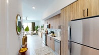 Located on NE First Ave in Dania Beach, Florida, Seaside Studio 531 is a thoughtfully designed studio that maximizes functionality and style within a single-floor open-concept layout. The space is finished with large-format light tile flooring throughout, contributing to a clean, cohesive aesthetic bathed in natural light.

The kitchen is a standout feature, equipped with full-height wood-tone cabinetry, stainless steel appliances including a refrigerator, electric range, built-in microwave, and dishwasher, as well as light quartz countertops and a subway tile backsplash. The generous cabinetry provides ample storage for a studio setting.

The open living and sleeping area offers a versatile layout, with the sleeping zone and living space separated by an open shelving unit that adds visual depth without closing off the room. A ceiling fan overhead ensures comfort year-round. A sliding glass door opens to a private balcony, allowing abundant natural light and outdoor views.

The bathroom is well-appointed with a wood-tone vanity, quartz countertop, a walk-in marble-tiled shower with a louvered door, and clean white walls that keep the space feeling bright and fresh. The overall ambiance is modern and airy, ideal for comfortable living in South Florida.