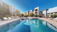 Located at 3310 S Kenton St in Denver, Colorado, this resort-style pool area offers an expansive and well-appointed outdoor retreat. The centerpiece is a generously sized swimming pool with crystal-clear blue water, featuring a gradual entry with in-water sun loungers that allow residents to relax at the water's edge. The pool deck is finished in smooth concrete and lined with an abundance of modern white chaise lounges and side tables, providing ample space for sunbathing under the Colorado sky.

A separate hot tub area is situated adjacent to the main pool, surrounded by additional lounge seating and mature landscaping that provides a sense of privacy and tranquility. Shaded outdoor dining areas with umbrella-covered tables and chairs offer a comfortable space for gathering and socializing. A pergola-covered seating zone adds architectural interest and additional shade on sunny days.

The entire pool area is enclosed by a wrought-iron security fence with a gated entry, accented by colorful planters and manicured shrubs. Mature trees and verdant greenery are thoughtfully integrated throughout, softening the hardscape and enhancing the resort ambiance. The surrounding multi-story building features contemporary architecture with neutral tones, large windows, and private balconies that overlook this inviting outdoor amenity space.