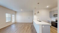 This thoughtfully designed single-floor residence offers a comfortable and modern living experience within a well-utilized footprint. The open-concept living, dining, and kitchen area forms the heart of the home, anchored by a sleek kitchen peninsula with a white quartz countertop, an undermount sink, and stylish brushed gold pendant lighting. The kitchen is outfitted with gray shaker-style cabinetry, stainless steel appliances including a refrigerator, range, and over-the-range microwave, and light wood-look flooring that flows seamlessly throughout the main living areas. The living room is bright and airy, featuring large windows with blinds, a ceiling fan, and access to an exterior door that welcomes an abundance of natural light. The bedroom is a comfortable retreat with plush carpeting, a ceiling fan, a window for natural light, and direct access to the bathroom. The full bathroom includes a tub and shower combo with tiled surround and brushed nickel fixtures. A dedicated laundry room houses a full-size washer and dryer alongside overhead wire shelving for added storage. Two closets provide further organizational space, completing this efficient and modern single-floor layout.