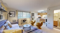 This well-organized one-bedroom, one-bathroom unit makes smart use of its compact footprint across a single floor. The open-concept main area seamlessly blends the living and sleeping spaces, creating a versatile and functional environment. A bold yellow accent wall anchors the bedroom area, adding warmth and personality, while a large window fitted with blinds invites ample natural light throughout the day. The living space accommodates a seating arrangement alongside a dedicated desk nook, offering both comfort and practicality.

The kitchen is positioned at one end of the main living area and features warm honey-toned wood cabinetry, a white electric range, a double-basin sink, and a full-size refrigerator. Light tile flooring and under-cabinet lighting contribute to a clean, functional cooking space with adequate storage.

The bathroom retains a classic aesthetic with white subway tile lining the walls of the shower-tub combination, complemented by a vintage-style yellow tub and matching fixtures. A wood-vanity cabinet with a wall-mounted medicine cabinet completes the space. Throughout the unit, the layout is thoughtfully arranged to maximize every square foot, making it a well-appointed and characterful living space.