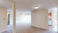 This single-floor residence offers a practical and straightforward layout designed for comfortable everyday living. The kitchen is efficiently arranged with warm honey-toned wood cabinetry providing generous upper and lower storage, dark granite-style countertops, and a full suite of white appliances including a refrigerator, dishwasher, and range. A window fitted with blinds over the sink brings in natural light, while durable tile-style flooring completes the space.

The living areas feature neutral-toned wall-to-wall carpeting and a soft, cream color palette that contributes to a bright and open feel. Large windows dressed with sheer curtains allow natural light to fill the main living space. A subtle step-down detail between areas adds architectural interest to the floor plan.

The bedrooms are well-proportioned, each carpeted and finished in warm neutral tones. A standout feature is the dual closets found in at least one bedroom, offering double the storage capacity with bifold doors providing easy access to built-in hanging rods and shelving.

The bathroom is cleanly appointed with a full-size soaking tub and shower combination featuring white subway tile surround, chrome fixtures, a wood-toned vanity, and warm tile flooring, creating a tidy and functional space.