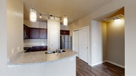 Located at 9233 Westridge Blvd in McKinney, Texas, this single-story residence offers a well-appointed interior with a consistent neutral color palette and a practical, open layout. The living area features dark hardwood-style flooring and a ceiling fan with light fixture, while multiple windows dressed with horizontal blinds allow natural light to fill the space. A door leads out to an exterior access point, enhancing the sense of openness.

The kitchen is a standout feature, anchored by a curved granite-topped breakfast bar peninsula with an integrated sink. Rich dark cabinetry provides ample storage, complemented by granite countertops, stainless steel appliances including a refrigerator, electric range, and over-the-range microwave. Pendant lighting and a track light fixture add a polished finishing touch overhead.

The bedrooms are carpeted and include ceiling fans, natural light from windows, and generous closet space. The primary suite connects to a private bathroom featuring dark vanity cabinetry with granite counters, hardwood-style flooring, and a walk-in closet. A secondary bathroom includes a tiled tub-shower combination. Hallways and secondary spaces also feature the dark hardwood-style flooring, maintaining a cohesive look throughout.