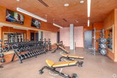 Located at 3775 Sixth Avenue in San Diego's 92103 neighborhood, this fitness center offers a generously sized, single-floor layout designed to accommodate a comprehensive range of workout experiences. The main gym floor is bathed in abundant natural light streaming through floor-to-ceiling windows that line the exterior walls, offering views of the surrounding San Diego streetscape and palm-lined outdoors. The warm-toned stucco ceilings, complemented by sleek linear pendant lighting, create an inviting yet energizing atmosphere throughout.

The primary workout area is outfitted with a broad selection of strength machines, free weights including a full dumbbell rack, adjustable benches, treadmills, and cardio equipment positioned to take advantage of the natural light and outdoor views. A dedicated strength zone features a power rack with weight plates, a cable machine, and open floor space for functional training, framed by large wall mirrors that enhance the sense of openness.

A separate cycling studio, enclosed by full-height glass walls, houses a row of stationary bikes facing a wall-mounted flat-screen display, with hardwood flooring adding warmth to the space. An additional training area provides selectorized machines, a rowing machine, dual wall-mounted televisions, and mirror-lined walls. The overall design balances functionality with a polished, modern aesthetic.