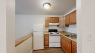 Located at 2206 N Berkshire Rd in Charlottesville, Virginia, this single-floor unit offers a well-organized and functional layout. The interior is finished with consistent wood-look flooring throughout, providing a warm and cohesive aesthetic across all areas.

The combined kitchen and living room serves as the heart of the unit. The kitchen features warm-toned wooden cabinetry, a countertop peninsula that opens toward the living area, a double sink, and full-size appliances including a refrigerator and range. The peninsula layout encourages an open flow between cooking and living spaces.

The living area is bright and airy, benefiting from large windows fitted with horizontal blinds that allow natural light to fill the room while offering privacy. A wall-mounted HVAC unit and baseboard heating provide year-round climate control. The neutral cream-colored walls and clean lines give the space a simple, understated character.

The bathroom is neatly appointed with a white vanity and mirror, a toilet, and a tiled bathtub/shower combination. Its light, neutral palette maintains the clean aesthetic found throughout the unit.

An in-unit laundry area adds a practical convenience. The unit also features a private entry door visible from the living room, with outdoor views of surrounding greenery through the windows.