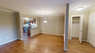 This single-floor residence offers a well-designed open-concept layout that seamlessly connects the main living areas. Warm hardwood flooring extends throughout the space, adding a sense of continuity and warmth to every room. The living and dining area is generously proportioned, anchored by a stylish pendant light fixture that serves as a focal point and provides ambient illumination. Crown molding along the ceiling adds a refined architectural touch throughout.

The kitchen is thoughtfully designed with rich, dark wood cabinetry that provides ample storage, complemented by a dark countertop breakfast bar that doubles as a casual dining or prep area. Stainless steel appliances, including a range and microwave, offer modern functionality. Pendant lighting over the bar area enhances both the aesthetic and practicality of the space.

A structural column near the living area adds an architectural element that subtly defines the transition between spaces. Neutral-toned walls throughout create a versatile backdrop suitable for a variety of interior styles. A doorway visible to the side hints at additional rooms, including what appears to be a closet or storage space. Overall, the residence presents a clean, functional, and inviting environment with classic design details.