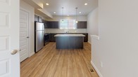 The Brixton is a three-story unfurnished residence designed with clean, contemporary finishes and a functional layout across all levels. The entryway greets residents with warm wood-look luxury vinyl plank flooring, crisp white five-panel doors, and brushed nickel hardware, establishing a cohesive modern aesthetic carried throughout the home.

The kitchen serves as a central highlight, featuring dark espresso cabinetry, granite countertops, a classic subway tile backsplash, and stainless steel appliances including a refrigerator, range, and microwave. A substantial kitchen island with pendant lighting above provides additional prep space and a natural gathering point, while recessed lighting and wood-look flooring complete the space.

Bedrooms are finished with plush neutral carpeting, ceiling fans, and windows that allow natural light to fill each room. Multiple bathrooms throughout the home are outfitted with dark cabinetry, granite-topped vanities, wood-look vinyl flooring, and large mirrors, offering both practicality and refined style. A convenient half bath is also present on one of the levels.

The overall ambiance of The Brixton is clean, modern, and move-in ready, offering a well-organized multi-story layout suited for everyday living.