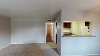 This single-story classic unit in Houston, TX offers a well-organized layout designed for comfortable everyday living. The living room is a generous, open space finished with neutral carpet and gray walls, illuminated by a ceiling fan with a light fixture. A pass-through counter connects the living area to the kitchen, offering a sense of openness between the two spaces. A window in the living room allows natural light to filter in, providing views of the surrounding greenery.

The galley-style kitchen is efficiently designed with dark espresso cabinetry lining both walls, granite-style countertops, a double stainless steel sink, a gas range, and a full-size refrigerator. Wood-style flooring runs throughout the kitchen, adding warmth and durability to the space.

The bedroom features rich, dark hardwood-style flooring, a ceiling fan, a window for natural light, and a closet with built-in shelving for ample storage. An additional smaller room off the bedroom provides further flexibility.

The bathroom includes a full tub-shower combination, a vanity with granite-style countertops, and classic tile flooring, maintaining a clean and functional aesthetic throughout.