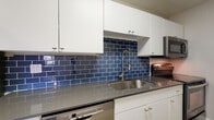 Located at 5615 N 7th St in Phoenix, AZ, this single-floor unit offers a thoughtfully updated interior with a clean, modern aesthetic throughout. Light wood-style flooring flows seamlessly across the living and kitchen areas, providing a warm and cohesive foundation for the space.

The kitchen is a standout feature, showcasing a striking deep blue subway tile backsplash that adds bold contrast against the white cabinetry and gray countertops. Stainless steel appliances — including a refrigerator, dishwasher, and range — are complemented by a brushed nickel pull-down faucet set within a single-basin sink, delivering a polished, functional workspace with generous cabinet storage above and below.

The open living area is bathed in a neutral palette, with textured ceilings and clean white baseboards framing the space. A dedicated bedroom features a ceiling fan with light fixture, a window that invites natural light and views of the surrounding greenery, and direct access to a bathroom. The bathroom includes a dark-toned vanity with an illuminated mirror and a full tub-shower combination finished in clean white tile surrounds.

Overall, the unit presents a well-maintained and updated interior that balances practical functionality with contemporary design touches, making it a comfortable and inviting space in central Phoenix.