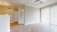 This single-floor residence offers a thoughtfully designed layout with a variety of functional spaces. The main living area is finished with distinctive light-toned herringbone-patterned flooring, crown molding, and a ceiling fan, creating a clean and polished aesthetic. A large sliding glass door fitted with vertical blinds allows abundant natural light to fill the space. The kitchen is efficiently organized with white cabinetry, stainless steel appliances including a range and microwave, a black refrigerator, and matching herringbone flooring that carries through from the main living area. A pass-through or bar counter connects the kitchen to the adjacent dining or living space. The bedroom features plush wall-to-wall carpeting, elevated ceilings, a ceiling fan, and direct access to a private bathroom. A second carpeted room also benefits from natural light through a sizable window and includes a built-in shelved walk-in closet, offering excellent storage. The bathroom is clean and functional, featuring a full soaking tub with a tiled surround and a shower, paired with herringbone-style flooring. Throughout, the neutral warm-beige color palette and consistent finishes lend the space a cohesive, move-in ready character.