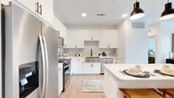 This single-story unit offers a thoughtfully designed layout that maximizes its compact footprint. The open-concept kitchen and living area serves as the heart of the home, where a bright, modern kitchen commands immediate attention. Crisp white shaker cabinets extend to the ceiling, providing generous storage, while a geometric hexagonal tile backsplash adds visual interest. A stainless steel farmhouse sink with a matte black faucet anchors the workspace, complemented by stainless steel appliances including a French door refrigerator, range, microwave, and dishwasher. A long waterfall-edge island with seating for several accommodates casual dining beneath sleek pendant lighting. Light wood-tone flooring flows throughout, enhancing the bright, airy atmosphere.

The living area features a ceiling fan, natural light from a large window, and direct access to an outdoor space via a glass-paneled door. The bedroom is a calm, well-lit retreat with a ceiling fan, a window with outdoor views, and ample room for a full furniture arrangement. An adjacent walk-in closet offers built-in shelving and hanging rods for organized storage. The full bathroom features a white vanity with undermount sink, matte black fixtures, a large mirror, and convenient access to a stacked in-unit washer and dryer.