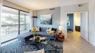 Located at 9888 E Vassar Dr in Denver, Colorado, this single-floor residence offers a well-appointed layout with modern design throughout. The living room serves as a welcoming centerpiece, featuring a tiled fireplace, a soothing blue-gray accent wall, and large sliding glass doors that open to a private balcony with views of surrounding greenery, allowing abundant natural light to fill the space. Light wood-style flooring flows consistently throughout the unit, enhancing the cohesive aesthetic.

The galley-style kitchen is efficiently designed with dark lower cabinetry contrasted by white upper cabinets, light countertops, and a window that brightens the space. A dedicated dining area adjacent to the kitchen features a solid wood table and is accentuated by a large floor-to-ceiling mirror wall that amplifies the sense of space.

Both bedrooms are generously sized, each with sliding glass door access to a balcony, soft accent walls, and ample room for furnishings. The primary bedroom offers a calm, inviting atmosphere with warm lighting and tree-lined outdoor views.

The bathrooms are cleanly finished with wood-look flooring, dark vanity cabinetry, white countertops, and a tiled shower-tub combination. One bathroom also features a soaking tub with a natural light window, adding a relaxing touch to the overall design.
