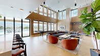 Located at 509 S Nevada Ave in Colorado Springs, CO, this striking single-floor communal living space is defined by its dramatic double-height ceilings and an abundance of natural light streaming through floor-to-ceiling windows. The expansive living room is anchored by a distinctive chevron-patterned hardwood floor that runs throughout, lending warmth and visual elegance to the open layout.

The lounge is thoughtfully furnished with a large sectional sofa in soft gray, accented by rust-orange velvet accent chairs that add a bold, contemporary touch. A sleek linear fireplace set into a textured white shiplap wall serves as a focal point, flanked by a large wall-mounted television and a built-in bookshelf displaying curated décor. Warm wood paneling lines the walls, complementing the natural tones of the interior.

A full-size shuffleboard table occupies a dedicated game area, while seating clusters offer flexible arrangements for socializing or relaxing. Floor-to-ceiling windows frame sweeping views of the Rocky Mountains and an adjacent outdoor pool terrace, seamlessly connecting the interior to the outdoors. The entry foyer features bold blue double doors, patterned accent wallcovering, and lush indoor greenery, setting a welcoming tone. The overall ambiance is modern, airy, and refined.