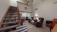 Located at 3900 Wyndover Dr in Springfield, Ohio, this two-story home is defined by its striking double-height living room, where soaring ceilings and an open upper loft area create a grand sense of vertical space. A wooden staircase with warm-toned balusters ascends from the main level, serving as a functional architectural centerpiece. The living area is carpeted and offers generous room for seating, with a convenient under-stair nook that adds practical storage or display space.

Adjacent to the living room, a dedicated dining area features wood-look flooring and connects to the galley-style kitchen. The kitchen is well-appointed with warm wood cabinetry, granite-look countertops, a double sink, gas range, and full-size refrigerator, offering ample storage and workspace.

Two bathrooms serve the home, each featuring wood vanities with granite-look counters and wood-look flooring. One includes a shower-tub combination. The bedrooms are carpeted and comfortable in scale, with ceiling fans providing airflow. One bedroom has direct access to a bathroom, enhancing functionality. Throughout, the home maintains a neutral palette with warm wood accents, creating a cohesive and welcoming atmosphere across both floors.