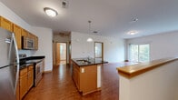 Located at 2950 Clearwater Ln in Waukesha, Wisconsin, this well-appointed one-bedroom, two-bathroom home offers a functional and comfortable layout across a single floor. The open-concept kitchen and living area serves as the heart of the home, featuring warm hardwood flooring, rich wood cabinetry, dark granite countertops, and a central island with a built-in sink. Stainless steel appliances — including a refrigerator, range, and microwave — provide a modern touch, while pendant lighting above the island adds a refined detail. The living area extends naturally toward a patio, offering outdoor access and natural light. The spacious primary bedroom is finished with plush carpeting, two closets, and a window that frames views of the surrounding greenery. The primary bathroom is bright and clean, featuring tile flooring, a wood vanity with a white countertop, and a window that fills the room with natural light. A second bathroom with laundry facilities adds everyday convenience. A carpeted staircase with a wood handrail connects to the entry level below. Throughout, warm wood trim and neutral tones create a cohesive and inviting atmosphere.