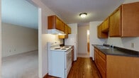 This single-floor unit offers a practical and well-organized layout across several distinct living areas. The galley-style kitchen is a functional centerpiece, featuring warm honey-toned wood cabinetry on both sides, dark granite-style countertops, hardwood-style flooring, and white appliances including an electric range and refrigerator. An under-cabinet range hood and ample upper and lower cabinetry provide solid storage and workspace. A hallway visible from the kitchen connects to additional rooms, maintaining an efficient flow throughout the unit.

The living area is generously proportioned, finished with neutral carpet and a textured ceiling. A large sliding glass door floods the space with natural light and opens to a balcony with outdoor views. Baseboard heating runs along the perimeter, a practical feature consistent throughout the unit.

The bedrooms are carpeted and include windows with blinds offering outdoor views, along with sliding-door closets providing convenient storage. One bedroom also features baseboard heating.

Two bathrooms serve the unit. The full bathroom includes a tub-shower combo, toilet, and a vanity with a granite-style countertop and wood cabinetry. The half bathroom mirrors the same vanity style with a white cabinet and matching countertop, finished with tile flooring.