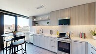 This thoughtfully designed one-bedroom, one-bathroom residence offers a contemporary urban living experience within a compact and efficient single-floor layout. The open-concept living and kitchen area serves as the heart of the home, bathed in natural light from large, floor-to-ceiling windows that frame impressive city skyline views. The living room provides generous space for comfortable seating arrangements and features light hardwood flooring that runs throughout the unit, contributing to a cohesive and modern aesthetic.

The kitchen is outfitted with light wood cabinetry, open display shelving, white quartz countertops, a stylish hexagonal tile backsplash, and stainless steel appliances including a range, microwave, and dishwasher. A breakfast bar adds additional functionality to the space.

The bedroom is a well-proportioned retreat featuring warm, neutral tones, recessed lighting, and access to a dedicated closet. It offers a calm and restful ambiance that complements the energetic urban views found elsewhere in the unit.

The full bathroom is clean and modern, showcasing light wood vanity cabinetry, a white countertop, large-format tile flooring, and matte black fixtures that add a refined contemporary touch. The overall design of the residence balances sleek, minimalist finishes with a warm and inviting atmosphere throughout.