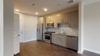 Located at 1399 Herrington Rd in Lawrenceville, GA, this Type A1A residence offers a thoughtfully designed single-floor layout with one bedroom and one bathroom. The open-concept living and kitchen area is anchored by rich, dark hardwood-style flooring that flows throughout the main living spaces, creating a cohesive and modern aesthetic. The kitchen is well-appointed with light wood grain cabinetry extending to the ceiling for ample storage, a full suite of stainless steel appliances including a gas range, over-the-range microwave, refrigerator, and dishwasher, complemented by granite countertops and a subtle subway tile backsplash. The living area benefits from natural light through a large window and is outfitted with a ceiling fan. The bedroom features plush carpeting and a generously sized window offering outdoor views of the surrounding greenery. The bathroom is finished with a granite-top vanity with wood cabinetry, subway tile surrounding the tub/shower combo, and the same hardwood-style flooring. Clean neutral wall tones, recessed lighting, and modern fixtures throughout lend this residence a polished, contemporary feel.