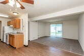This single-floor residence offers a functional and well-organized layout designed for comfortable everyday living. The open-concept kitchen and living area serves as the heart of the unit, where warm honey-toned wood cabinetry lines both sides of the galley-style kitchen, complemented by laminate wood flooring, a double-basin sink, and white appliances including a refrigerator, electric range, and dishwasher. A ceiling fan with a light fixture overhead enhances airflow in this shared space, which transitions seamlessly into a carpeted living area. A large sliding glass door floods the living room with natural light and provides views of the surrounding exterior. Multiple bedrooms feature plush carpet flooring, neutral walls, and windows that invite additional natural light. One bedroom benefits from direct access to both a walk-in closet and a private en-suite bathroom, adding a layer of convenience. The full bathroom includes a tub-shower combination, toilet, and vanity with a mirror. Throughout the unit, textured ceilings, dark wood door trim, and consistent neutral tones create a cohesive and understated aesthetic.