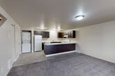 This two-story home in Lakewood, Washington offers a practical and well-organized layout across two evenly distributed floors. The main level features an open-concept living and kitchen area, where rich dark-espresso cabinetry contrasts cleanly against light countertops and white appliances, including a refrigerator, electric range, dishwasher, and a peninsula that defines the space. Light wood-look vinyl flooring runs through the kitchen, transitioning to plush carpet in the living area. A stacked washer and dryer unit is conveniently tucked on the main floor. A large window at the front of the living area allows natural light to flow in, and a staircase leads to the upper level. Upstairs, two carpeted bedrooms provide comfortable retreats, each with windows offering natural light. The primary bedroom is generously sized, with ample room for furnishings, while the second bedroom is well-suited as a guest room or home office. Two closets provide storage throughout the home. The full bathroom features a combined tub and shower with a handheld showerhead, a dark-vanity with a light countertop, and wood-look tile flooring, completing the home's consistent, modern aesthetic.