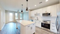 Located at 11830 Buckfield Cir in Jacksonville, FL, this efficiently designed 740-square-foot, single-floor unit offers 1 bedroom, 1 bathroom, and a versatile den across a thoughtfully laid-out floor plan. The open-concept kitchen is a standout feature, showcasing white shaker cabinetry with matte black hardware, a white quartz countertop island with pendant lighting, a subway tile backsplash, and a full suite of stainless steel appliances including a French door refrigerator, range, built-in microwave, and dishwasher. Light wood-look flooring flows seamlessly through the main living areas, complemented by recessed lighting and abundant natural light from multiple windows. The living room and den provide flexible living space, while a sun-filled bonus area features a glass exterior door and multiple windows. The 150-square-foot primary bedroom includes plush carpet, a ceiling fan, and access to a spacious walk-in closet with wire shelving. The bathroom features a dual-sink vanity with a white quartz countertop, gray cabinetry, a large mirror, and wood-look tile flooring. A dedicated laundry area with a stacked washer and dryer completes this well-appointed home.