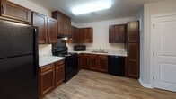Located at 5002 Strauss Ct in Fredericksburg, Virginia, this single-floor unit offers a practical and well-appointed layout with consistent finishes throughout. The kitchen is a standout feature, showcasing rich dark-stained cabinetry in an L-shaped configuration paired with light granite countertops. Black appliances — including a refrigerator, electric range, microwave, and dishwasher — complement the cabinetry, while wood-look plank flooring ties the space together. A double-basin sink sits beneath overhead cabinets, maximizing storage and functionality.

The open area adjacent to the kitchen provides versatile living space, illuminated by a classic chandelier and featuring a set of double doors for added storage. The bedrooms are carpeted and each include ceiling fans with lighting, offering comfort year-round. Windows in each bedroom allow natural light and neighborhood views.

Two bathrooms serve the unit — one featuring a full tub-shower combination with chrome fixtures, and a second with grab bars and a granite-topped vanity, both finished with wood-look flooring. Neutral wall tones and clean white trim carry throughout, creating a cohesive and move-in-ready environment.