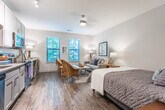 Located in Mount Pleasant, South Carolina, this single-floor studio offers a thoughtfully designed open-concept layout that seamlessly integrates living, sleeping, and dining functions into one cohesive space. Rich wood-look flooring flows throughout the main area, lending warmth and continuity to the interior.

The living and sleeping zone is generously proportioned, accommodating a full-size bed alongside comfortable seating and a sitting area. Two large windows dressed with horizontal blinds invite abundant natural light and frame views of lush surrounding greenery, creating a serene, nature-connected atmosphere. A ceiling fan adds both function and charm to this central space.

The kitchen is clean and contemporary, outfitted with crisp white shaker-style cabinetry, a subway tile backsplash, light countertops, and a full suite of stainless steel appliances including a range, microwave, and dishwasher. Light wood-look flooring in the kitchen complements the overall neutral palette.

The bathroom is finished with large-format tile flooring, a vanity with ample storage, a full mirror, and a shower-tub combination. Adjacent to the bathroom, a dedicated closet space with built-in shelving provides practical storage. The overall aesthetic throughout is calm and neutral, with soft gray and beige tones creating a relaxing, move-in-ready environment.