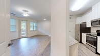 Located at 308 Mohegan Ave in Bluffton, SC, this single-story, one-bedroom, one-bathroom residence offers a thoughtfully designed layout with a clean, modern aesthetic throughout. The open-concept living area is bright and welcoming, featuring light wood-style plank flooring, neutral white walls, and a ceiling fan. Large windows fitted with blinds allow generous natural light to fill the space, while a glass door provides direct access to a private balcony overlooking lush greenery. The kitchen is equipped with white shaker-style cabinetry, granite countertops, stainless steel appliances including a refrigerator, range, and microwave, and additional pantry storage behind double doors. Granite surfaces continue into the hallway area, providing extra counter space. The spacious primary bedroom features plush carpeting, a large window with outdoor views, and ample room for furnishings. The bathroom is finished with white cabinetry, granite countertops, an undermount sink, a large vanity mirror, and a full tub-shower combination. Consistent finishes of granite and white cabinetry unify the space, creating a cohesive and polished living environment ideal for comfortable everyday living in the Lowcountry of South Carolina.