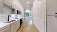 Located at 900 E Colorado Blvd in Dallas, TX, this thoughtfully designed one-bedroom, one-bathroom unit offers a clean, modern aesthetic across a single floor. Light wood flooring flows throughout, complementing the crisp white walls and trim that give the space a bright, airy feel.

The galley-style kitchen is well-appointed with white shaker cabinetry featuring matte black hardware, white subway tile backsplash, stainless steel appliances including a range, microwave, and refrigerator, and sleek white countertops. A dedicated pantry provides additional storage. The kitchen opens toward the living area, which benefits from large windows and glass doors that flood the space with natural light and offer views of the surrounding greenery.

The living room features notably tall ceilings and built-in open shelving, adding both function and character. The bedroom offers a comfortable, private retreat with its own closet. A dedicated laundry area adds everyday convenience.

The bathroom is finished with large-format white tile flooring, a wood-toned floating vanity with a white countertop, matte black fixtures, a backlit mirror, and a glass-enclosed shower. The overall design balances clean modern finishes with warm natural accents, creating a cohesive and functional living environment.