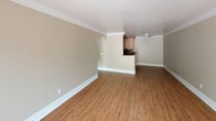 Unit #111 at 320 Pomelo in Vista is a well-appointed single-floor residence that combines comfort and functionality throughout its layout. The open living area is a standout feature, showcasing warm hardwood-style flooring, crown molding, and crisp white baseboards that lend a clean, polished look. A sliding glass door with vertical blinds fills the space with natural light while providing outdoor views, and a ceiling fan ensures year-round comfort. The kitchen is efficiently designed with rich wood cabinetry, granite-style countertops, a stone tile backsplash, and a breakfast bar that connects seamlessly to the living area. White appliances, including a refrigerator and range, are complemented by recessed lighting overhead. The bedroom offers plush carpeting, crown molding, a ceiling fan, and a large window with vertical blinds that invite natural light and greenery views. The bathroom features dark hardwood-style flooring, a wood vanity with a granite-top sink, a wall mirror, and a full bathtub with shower combination. Throughout the unit, consistent warm-toned walls and cohesive finishes create a comfortable and inviting atmosphere.