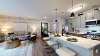 Located at 100 Oakview Dr in Trumbull, Connecticut, this single-floor residence offers a thoughtfully designed open-concept layout that seamlessly connects the kitchen, dining, and living areas. The kitchen is a standout feature, appointed with grey shaker-style cabinetry, white quartz countertops, a subway tile backsplash, stainless steel appliances including a gas range, and a generous central island with seating — all illuminated by stylish pendant lighting. Wood-look flooring flows throughout the main living spaces, enhancing the warm yet contemporary aesthetic. The living room is anchored by a striking textured accent wall and large sliding glass doors that open to a private balcony with outdoor views of the natural surroundings. A separate dining area provides an intimate space for entertaining. The bedroom features a bold geometric accent wall, natural light from a large window with outdoor views, and ample room for a king-sized bed. The bathroom is finished with light tile flooring, a grey vanity with white countertop, and clean, neutral tones. Throughout the residence, a cohesive palette of gold, grey, and green accents lends a refined, modern character to every room.