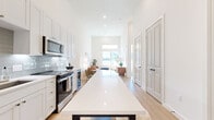 Located at 900 E Colorado Blvd in Dallas, TX, this thoughtfully designed 2-bedroom, 1-bathroom home offers a bright, modern aesthetic defined by a crisp white palette and light wood flooring throughout. The open-concept layout seamlessly connects the kitchen and living areas, creating an efficient yet airy flow. The kitchen is a standout feature, boasting tall white shaker cabinets, a subway tile backsplash, stainless steel appliances including a French door refrigerator and electric range, a wine cooler, and a long island with bar seating—ideal for dining and entertaining. Soaring ceilings in the kitchen and living area amplify the sense of space. The living room is bathed in natural light from large windows that offer open outdoor views, complemented by a transom window above for additional brightness. Both bedrooms are well-proportioned, with the primary bedroom featuring large windows with scenic views and direct access to the shared bathroom. The bathroom is finished with warm wood cabinetry, a white quartz countertop, a tiled walk-in shower, matte black fixtures, and a lighted mirror. Two closets and an in-unit laundry room add everyday practicality to this well-appointed Dallas home.