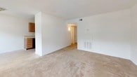 This single-floor, two-bedroom unit offers a straightforward and functional layout designed to maximize usable living space. The living area is generously sized, featuring neutral-toned wall-to-wall carpeting and crisp white walls that create a clean, open atmosphere. Multiple windows along the living room wall allow natural light to fill the space, enhancing its sense of openness. A built-in HVAC vent is integrated into the wall, ensuring efficient climate control throughout.

The kitchen is designed in a galley-style configuration, lined with warm-toned wood cabinetry on both upper and lower sections, offering ample storage. Light-colored countertops provide functional workspace, while appliances include a black dishwasher, a white electric range, and a full-size refrigerator. Tile flooring in the kitchen adds a practical, easy-to-maintain surface.

Both bedrooms are carpeted and feature white walls, with windows that bring in natural light and views of surrounding greenery. The rooms offer adequate space for standard bedroom furnishings.

The bathroom includes a full-size soaking tub with an overhead showerhead and chrome fixtures, finished with white tiled walls for a clean, classic appearance. Overall, the unit presents a practical and comfortable living environment with a neutral palette throughout.