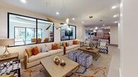 Located at 2900 N Braeswood Blvd in Houston, Texas, this single-floor leasing office and community lounge space showcases a sophisticated, contemporary design throughout. The interior is anchored by large-format neutral tile flooring that flows seamlessly across the open-plan layout, complemented by wood-tone flooring accents in transitional corridors.

The main lounge area is a standout, featuring generously sized cream sofas adorned with vibrant orange and patterned accent pillows, paired with patterned armchairs and geometric ottomans. Bold, sculptural gold pendant light fixtures serve as striking focal points overhead, while recessed lighting provides consistent, even illumination throughout. Large black-framed windows flood the space with natural light and offer views to the exterior, enhancing the open, airy ambiance.

A glass-partitioned conference or meeting room is visible from the lounge, furnished with a communal table and seating, ideal for private meetings or presentations. The entry corridor features crisp white walls adorned with a decorative geometric wood wall sculpture, a warm drum pendant light, and dark-framed doors that add architectural contrast.

A clearly marked leasing office area is accessible from the main corridor, ensuring a professional and welcoming experience for prospective residents. Overall, the space strikes a balance between functional professionalism and refined residential comfort.