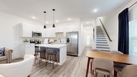 This well-designed two-story home offers a seamless blend of modern aesthetics and functional living. The main floor is anchored by a bright, open-concept kitchen featuring white shaker cabinets, a classic subway tile backsplash, quartz countertops, and a full suite of stainless steel appliances including a French door refrigerator, dishwasher, and range. A central island with a wood-toned base and bar seating serves as the heart of the space, complemented by stylish pendant lighting overhead. Light wood-tone flooring flows throughout, connecting the kitchen to the adjacent dining area and into the living spaces. The living room is generously sized with recessed lighting, a tray ceiling detail, and a clean, neutral palette that creates a calm and inviting ambiance. A staircase with contrasting dark treads connects the two floors with visual interest. Bedrooms are bright and comfortable, with natural light filtering through white-curtained windows. The bathroom is finished in crisp white tones with a full tub-shower combination. Throughout the home, clean white walls, recessed lighting, and light hardwood-style flooring create a cohesive, contemporary feel that is both welcoming and easy to maintain.